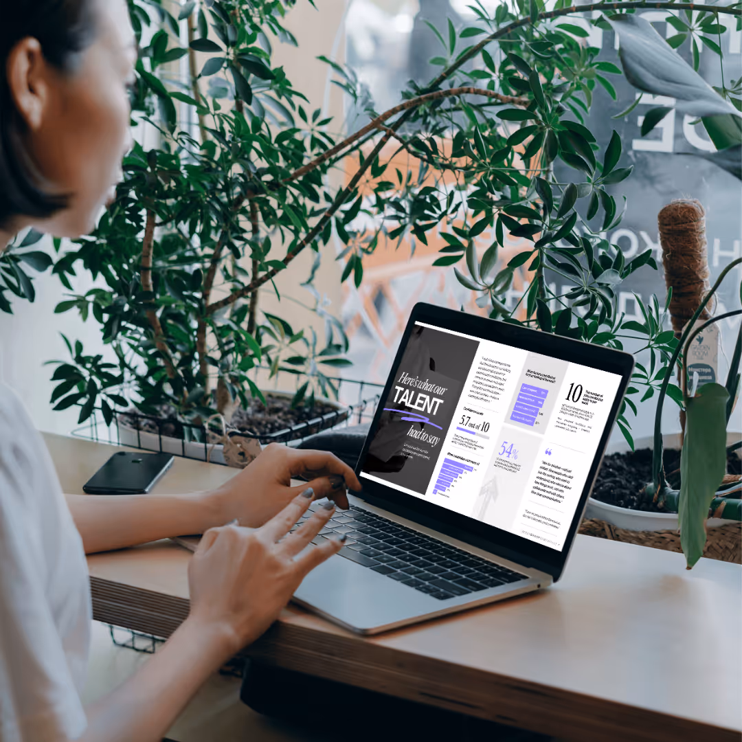 Woman in a suit, standing behind a reception desk, on the phone,  looking at a computer screen pleasantly. 