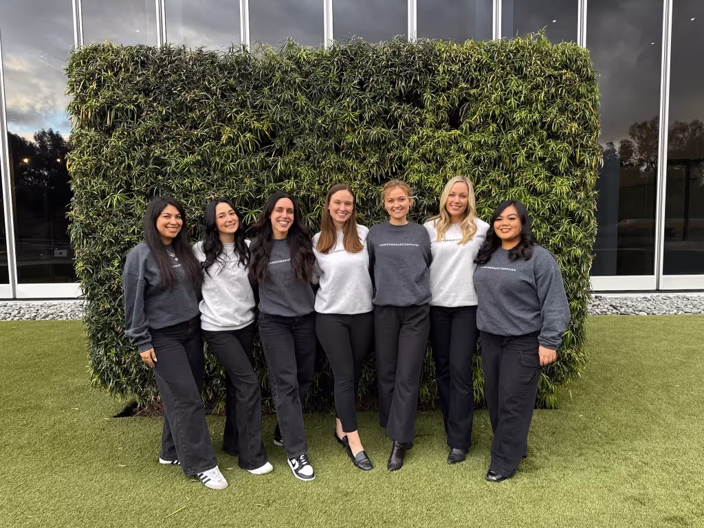 Modern, open-air room with floor-to-ceiling windows overlooking a calm ocean.   Wooden lounge chairs facing the water, with tall grasses near the edge.