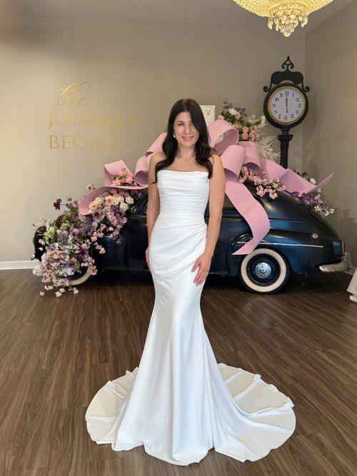 Bride modeling a sleek fit and flare wedding dress with dramatic train in Greenville South Carolina bridal boutique
