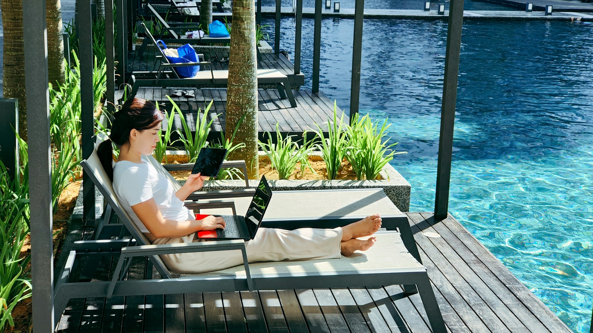 A woman sitting poolside while working on her laptop.