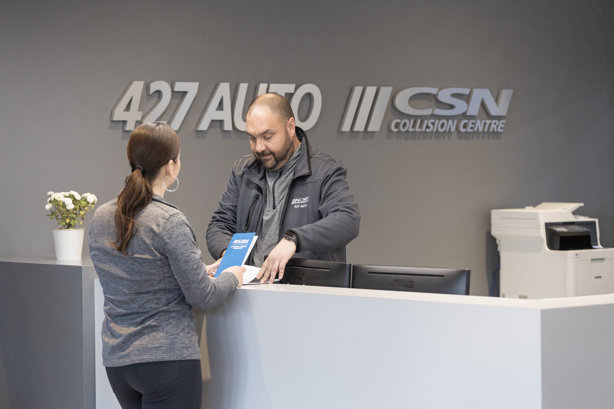 A customer at the front desk of CSN 427 Auto Collision in Etobicoke, under the 427 Auto CSN Collision Centre sign