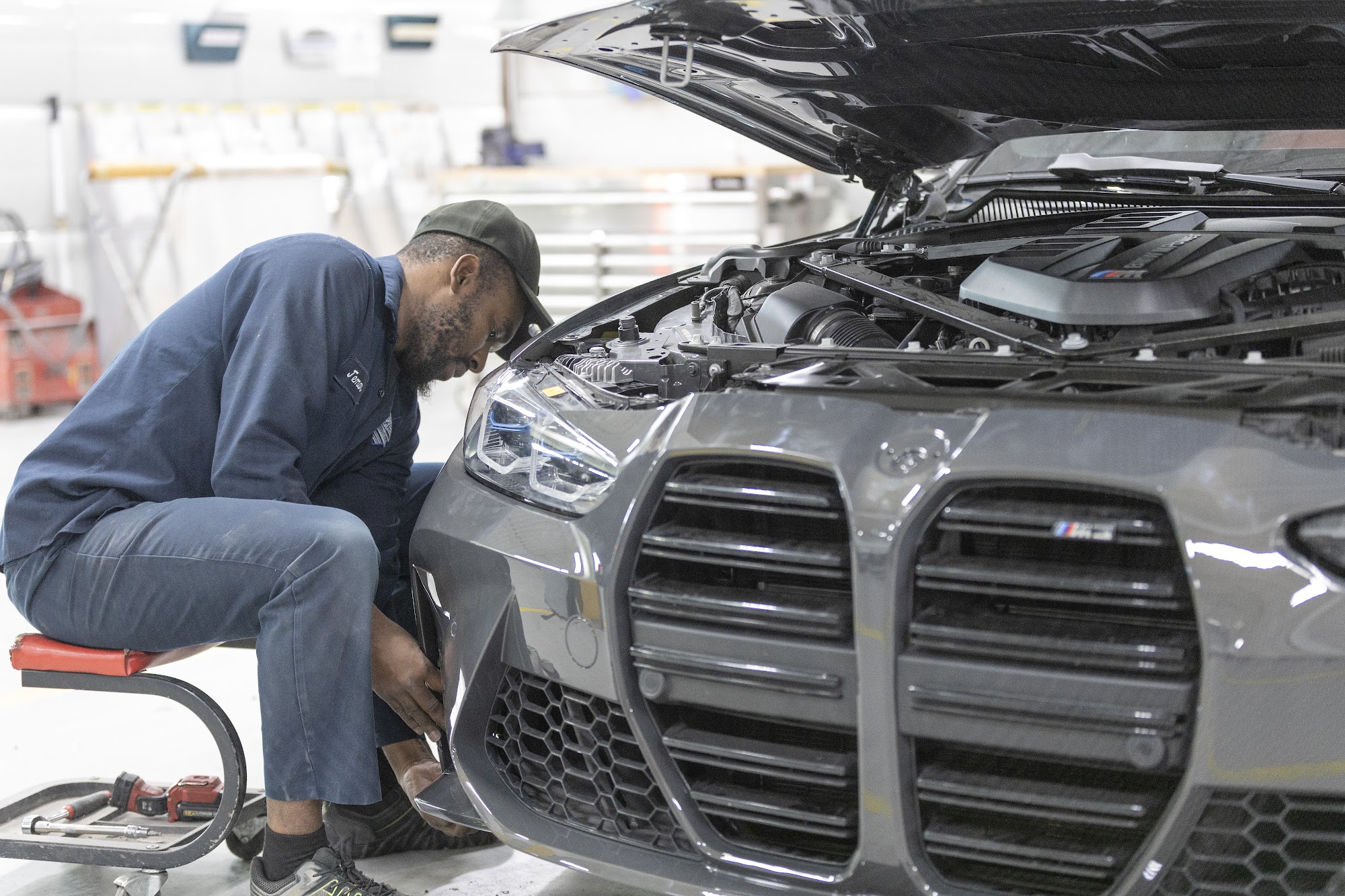 A CSN 427 technician works on the front bumper of a grey BMW M3 inside the Etobicoke collision centre