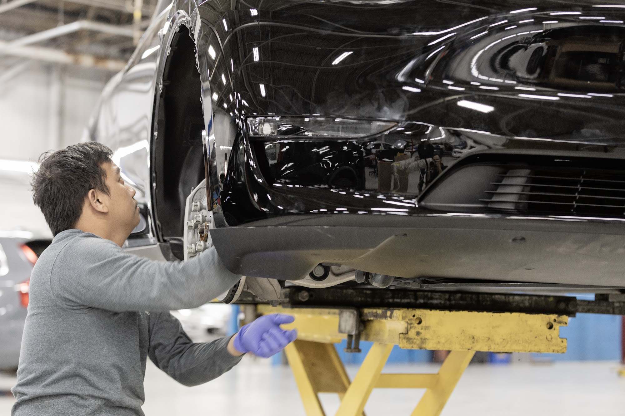 A CSN 427 Auto technician works on the rear structure of a black Tesla raised on a lift