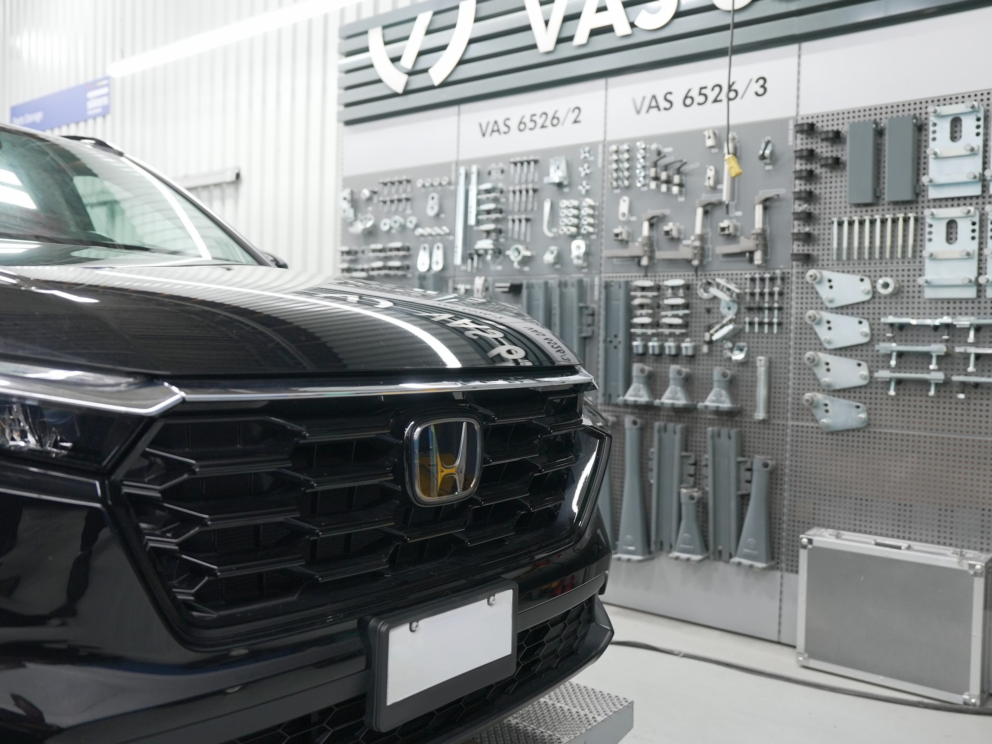 Front grille of a black Honda SUV in the collision shop, beside a wall of manufacturer repair tooling
