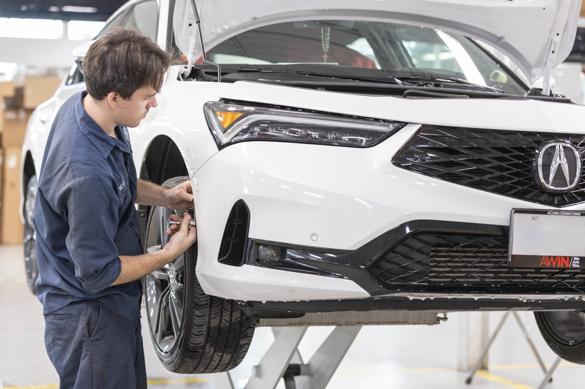 A CSN 427 Auto technician inspects the front bumper corner of a white Acura