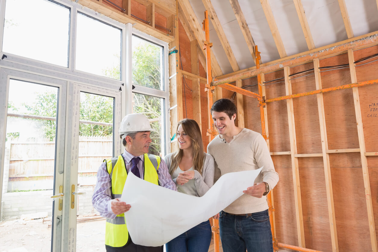 A home builder takes a young couple on a tour through a house in the framing stage of the build process.