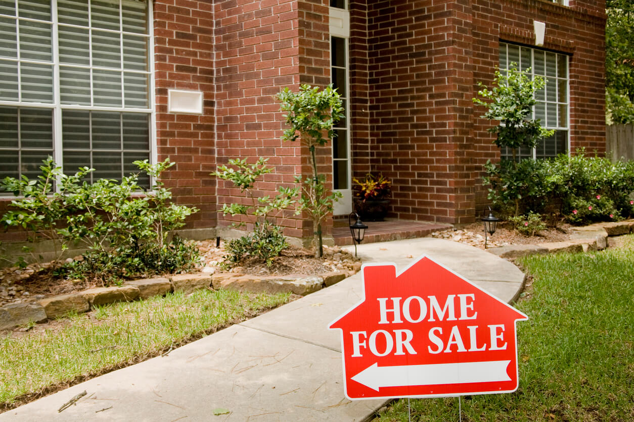 The entryway and for sale sign of an old brick home for sale in a suburb near Houston