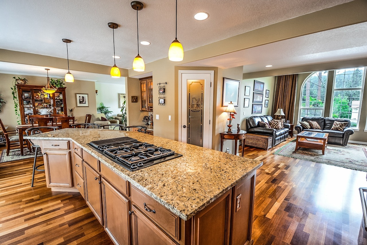 A photo of a home interior with a well-lit kitchen, dining room, and living room with couches.