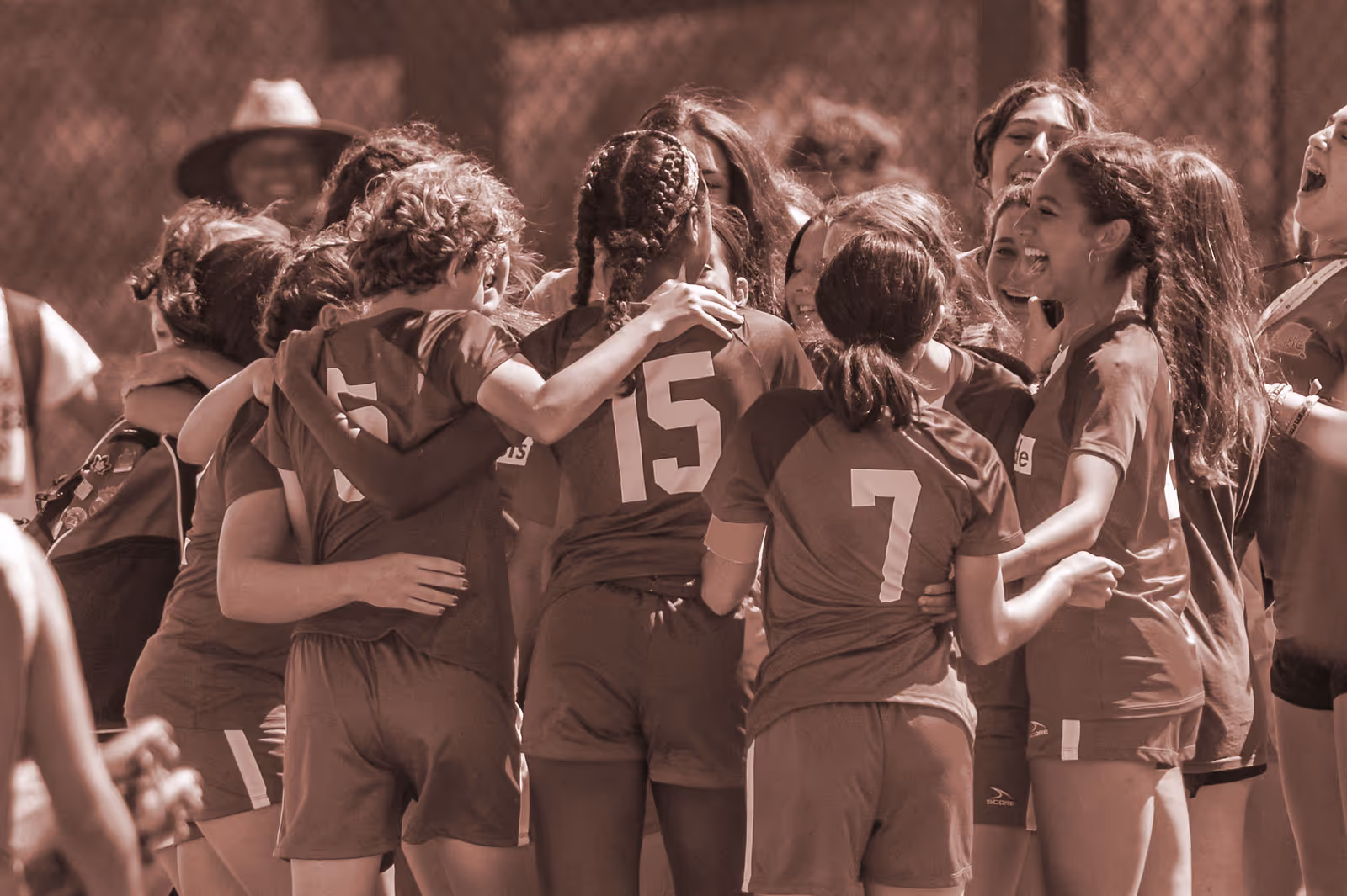 Group of young female soccer players in uniforms embracing and celebrating together.