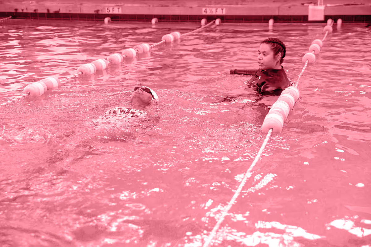 Swimming instructor in pool guiding a child floating on their back between lane dividers.