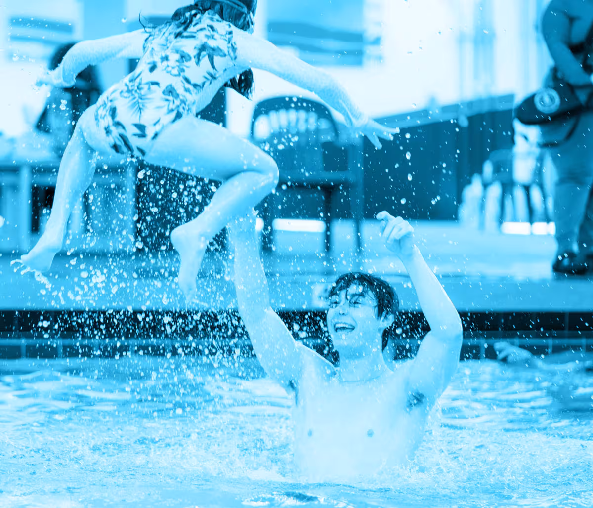 A man lifting a girl above water at a pool.