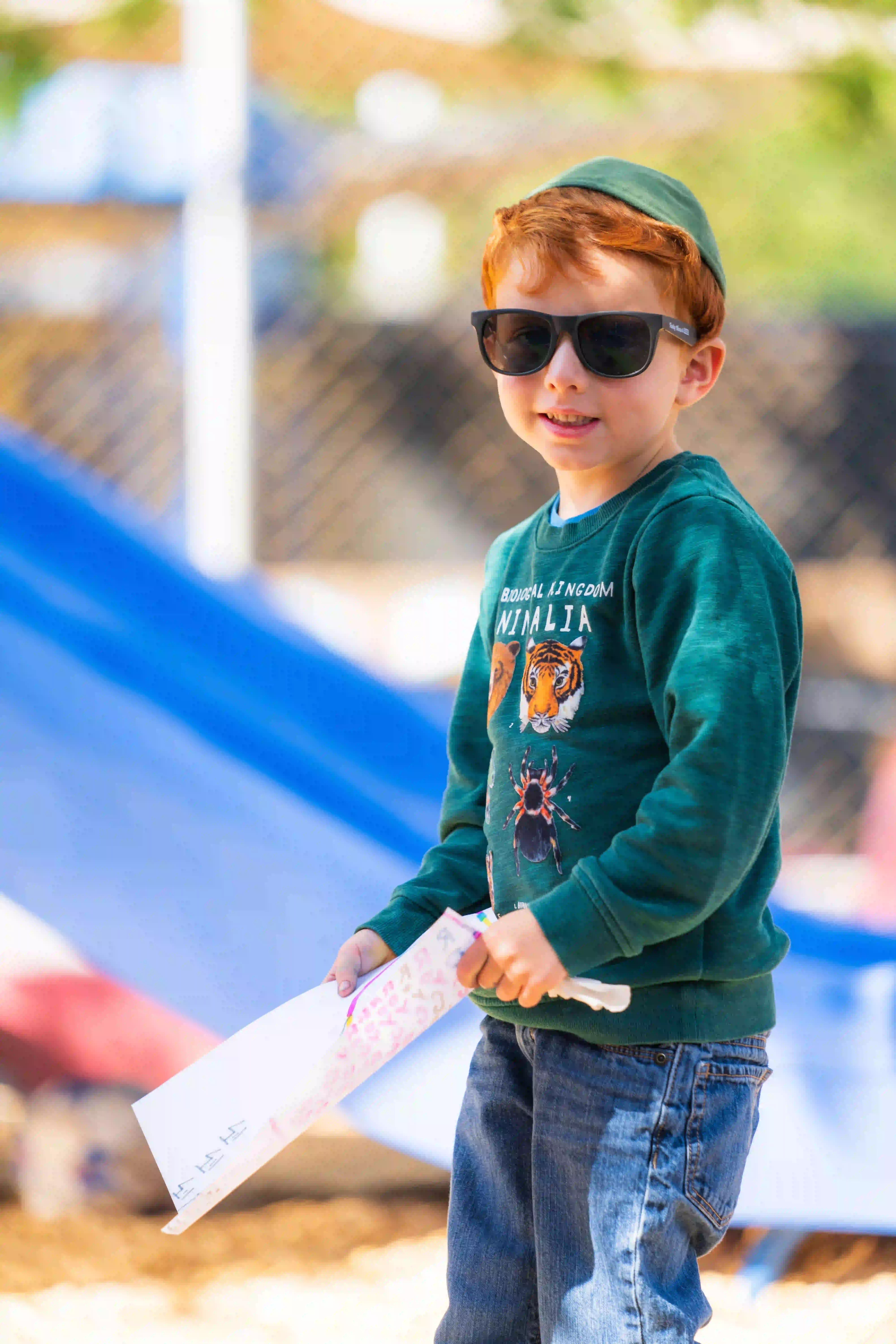 Child in sunglasses holding paper near playground at Jewish Preschool in Mid City Central Los Angeles.