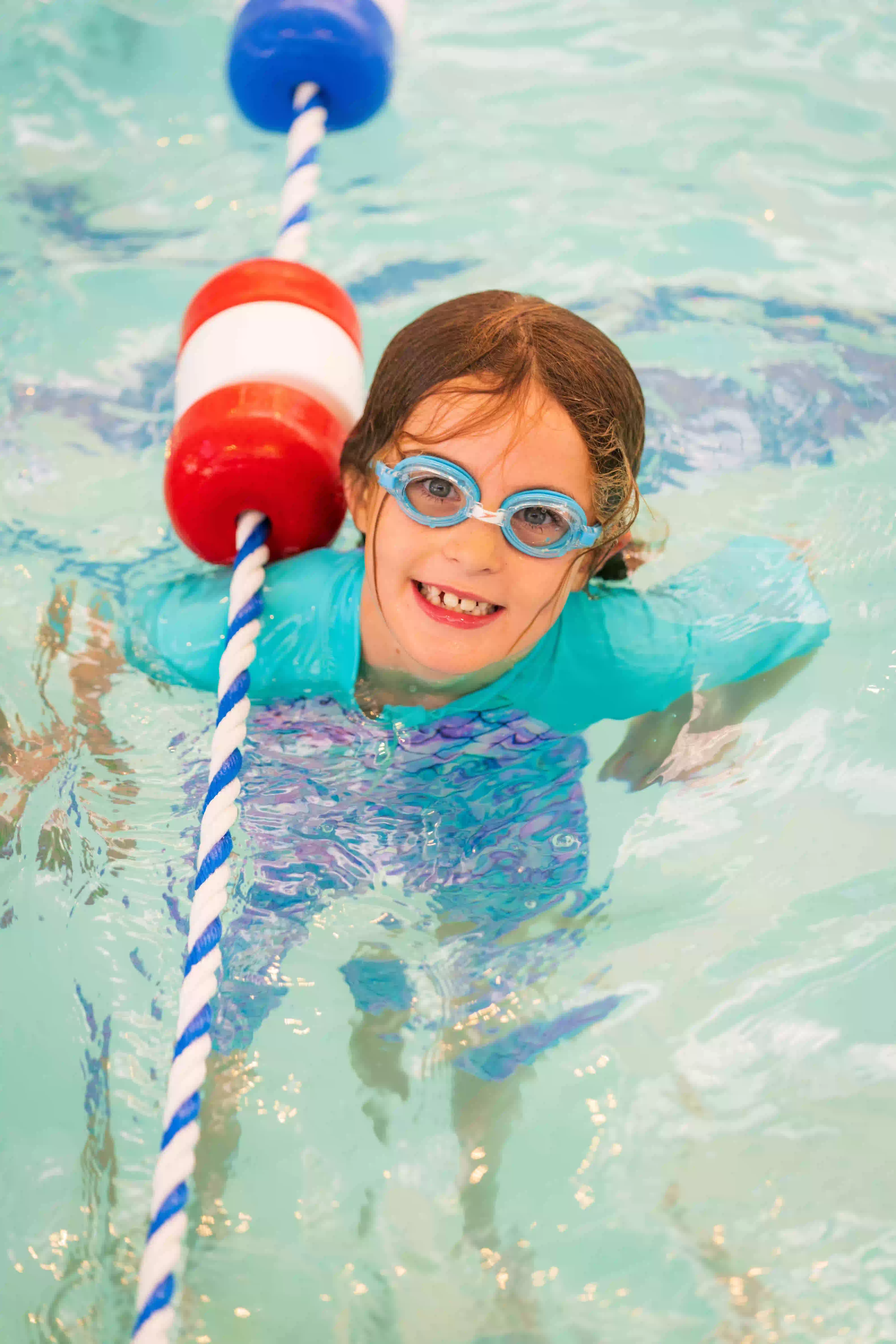 A girl wearing goggles floating in a pool.