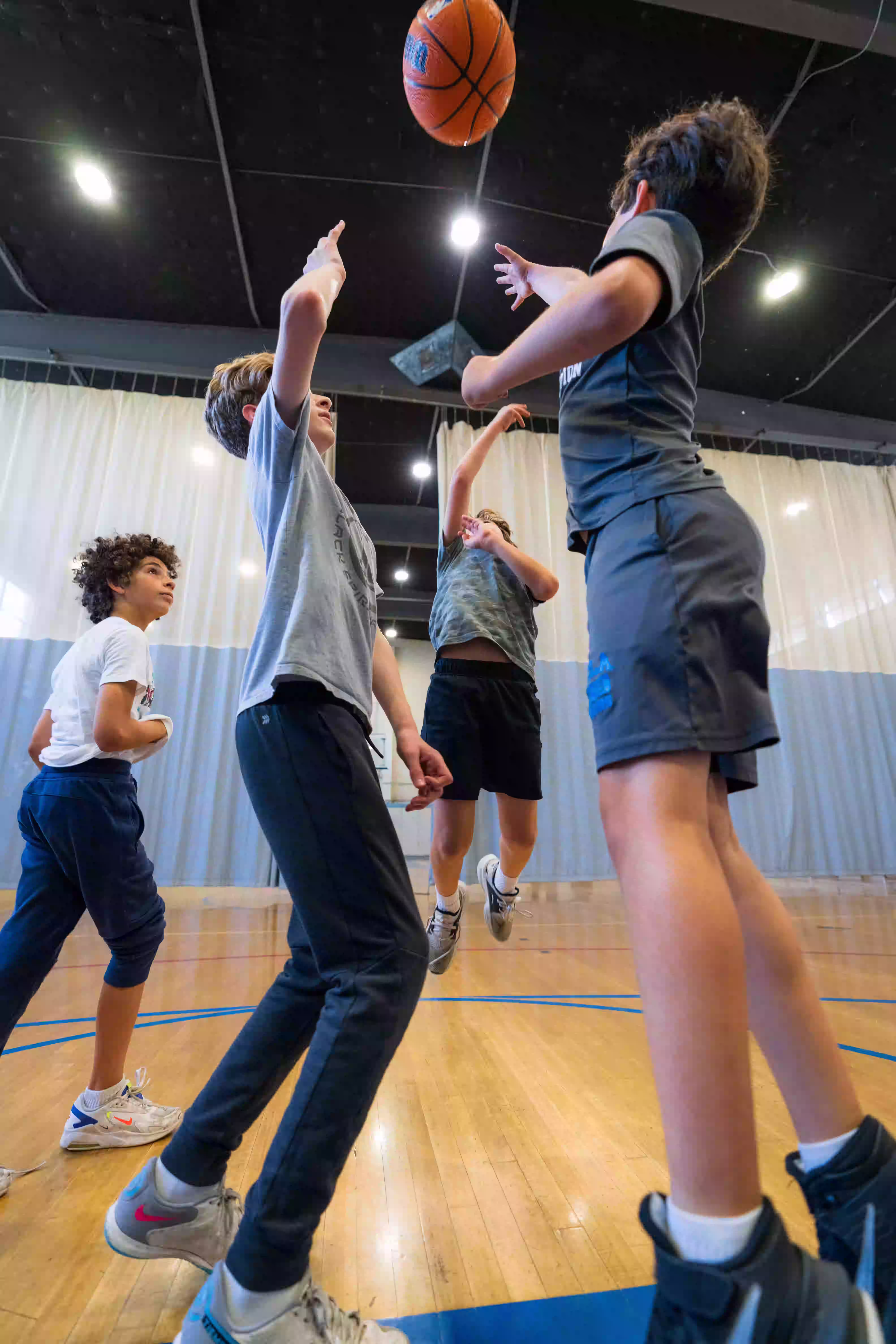 Four boys playing basketball indoors with one boy jumping to shoot the ball.