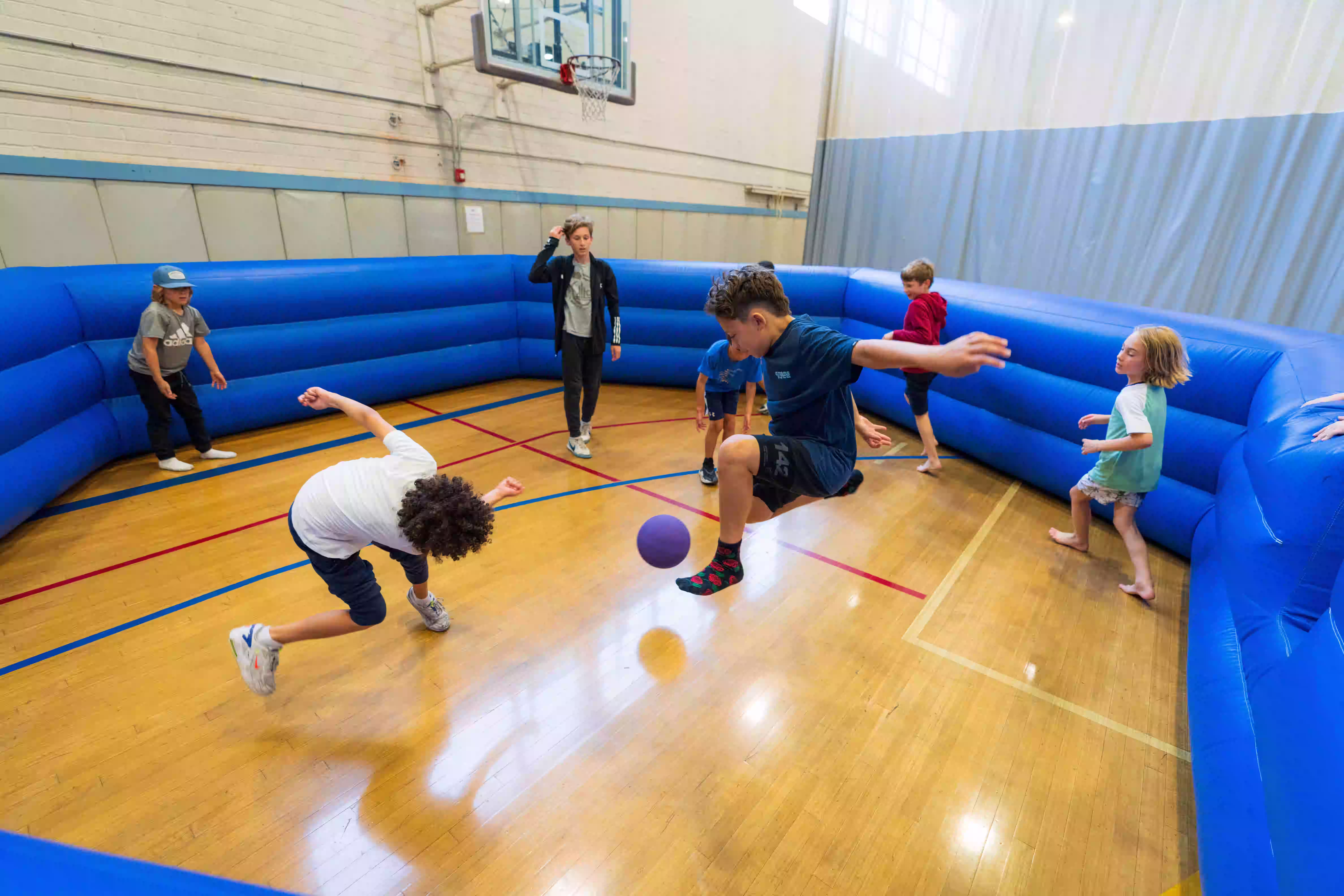 Children playing in an inflatable court with a purple ball.