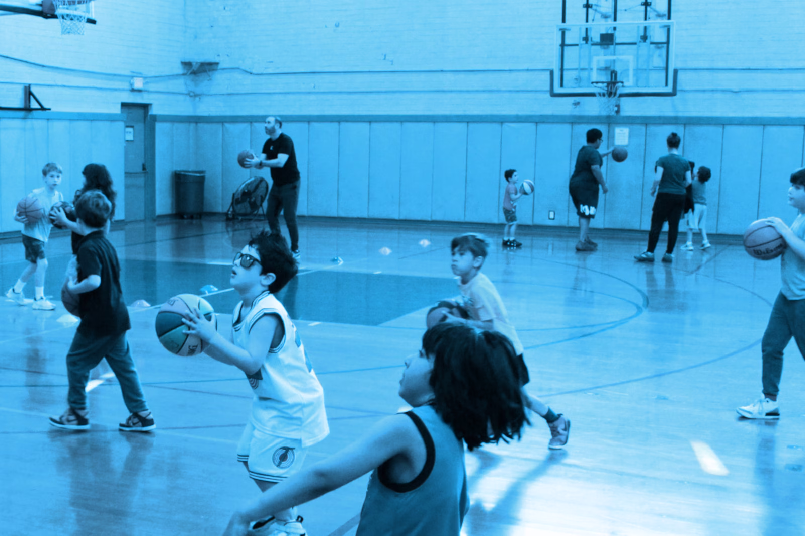 Children practicing basketball in a gym.