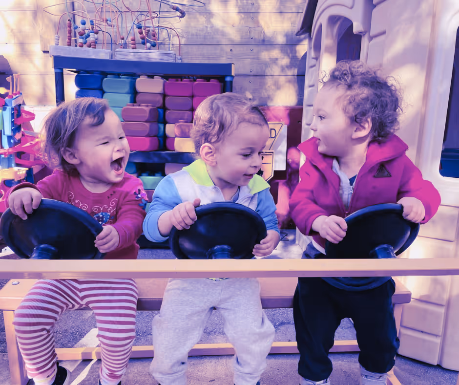 Three children playing with toy steering wheels at a playground.