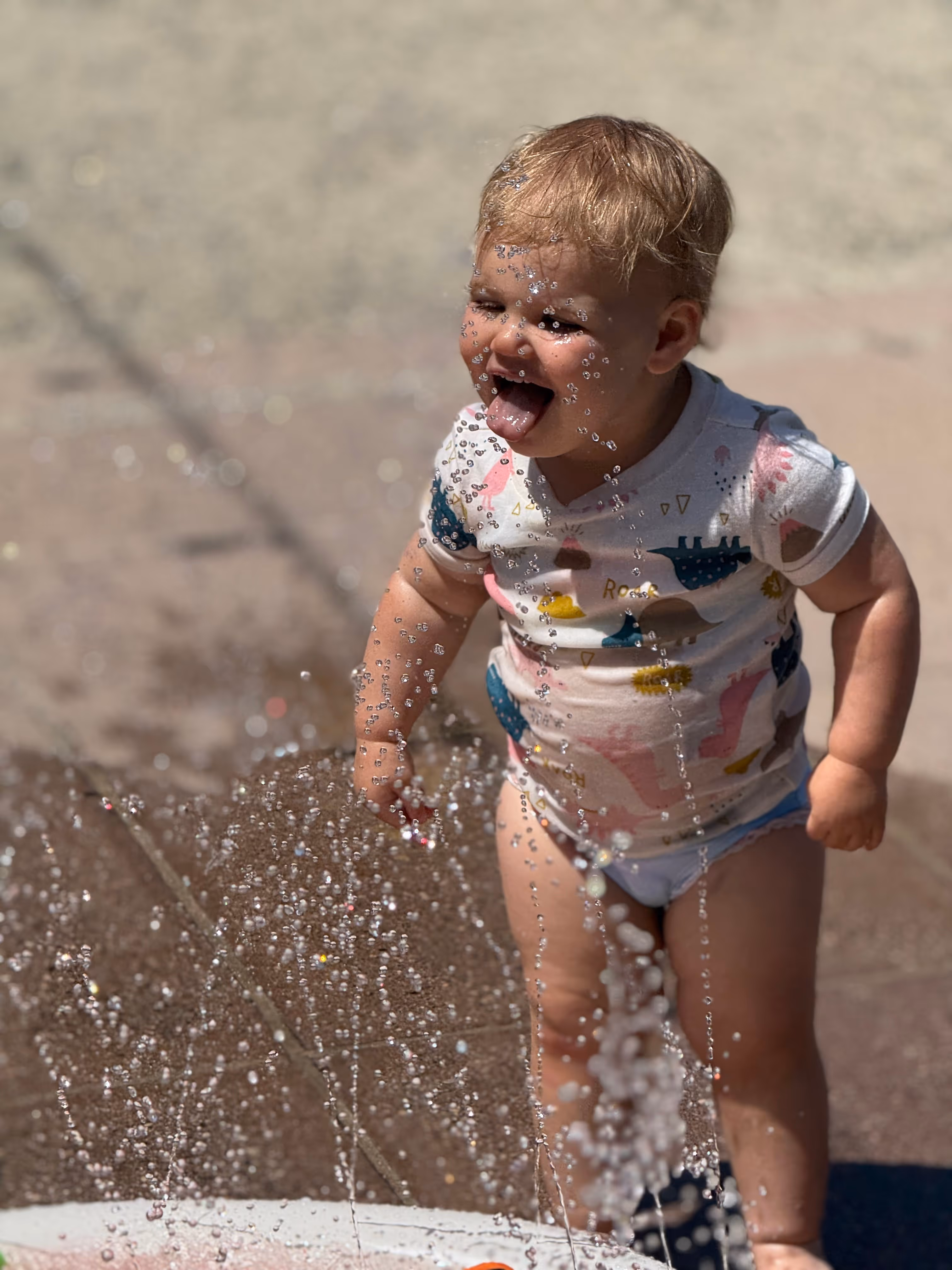 A toddler playing in water with a joyful expression.