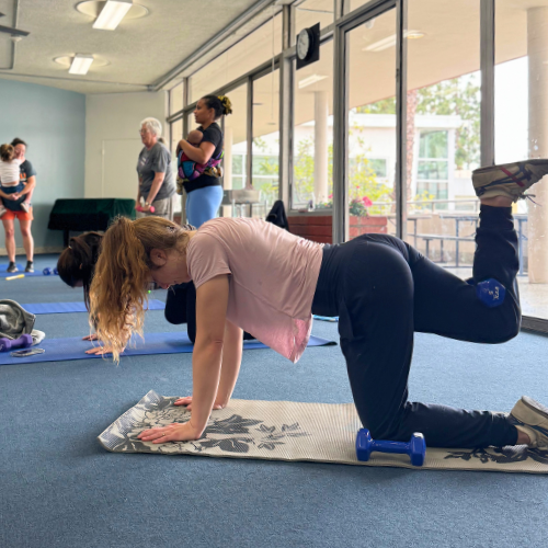 Adult in a core strengthening class working on a mat with a hand weight nearby.