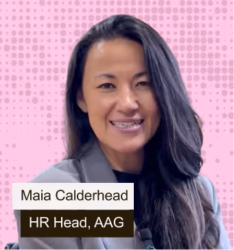 Portrait of Maia Calderhead smiling with long dark hair, wearing a gray blazer, against a pink dotted background.
