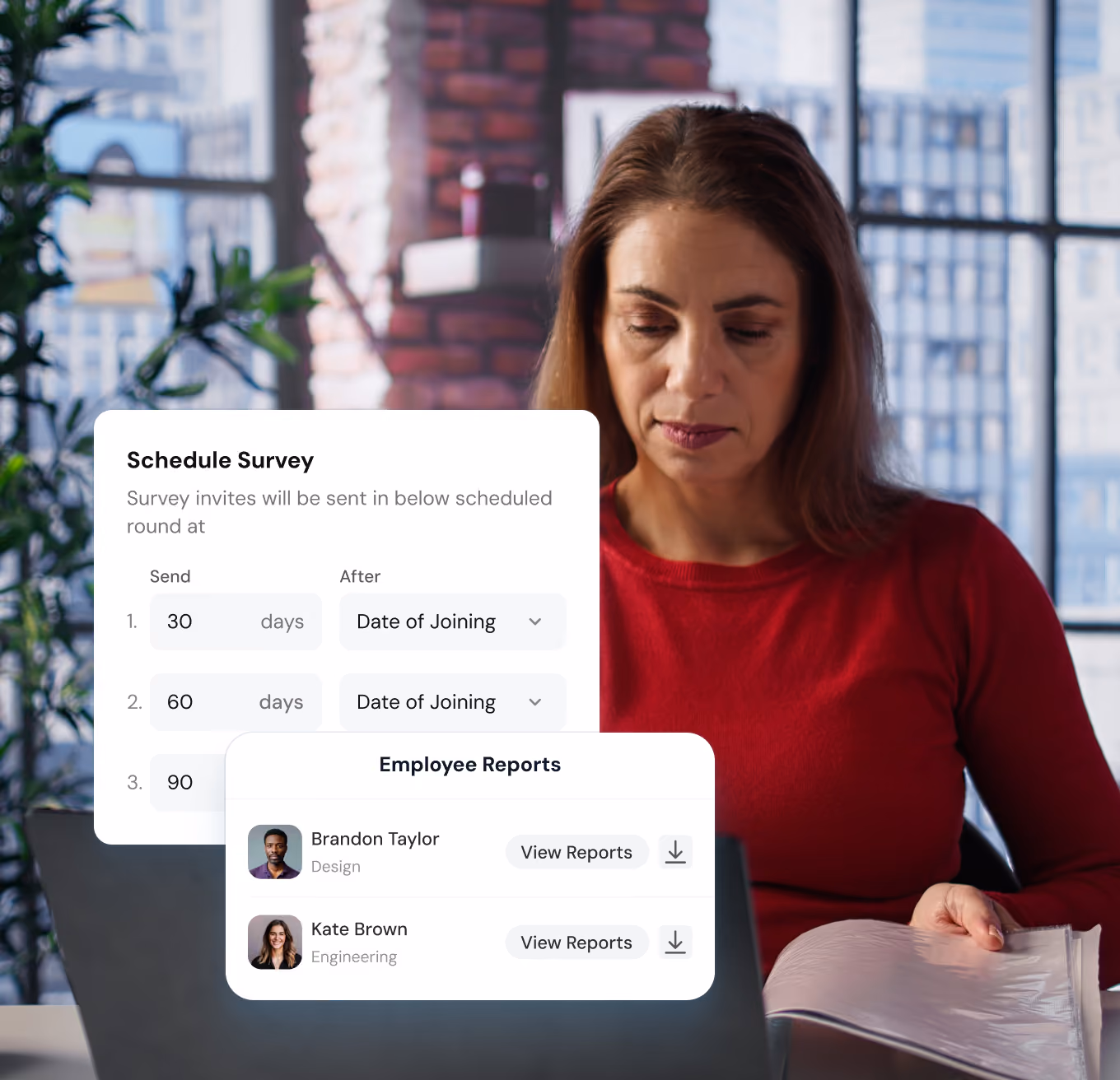 Woman in a red sweater working on a laptop in a brick-walled office with large windows, with screens showing a survey schedule interface and an employee reports list including names Brandon Taylor and Kate Brown.