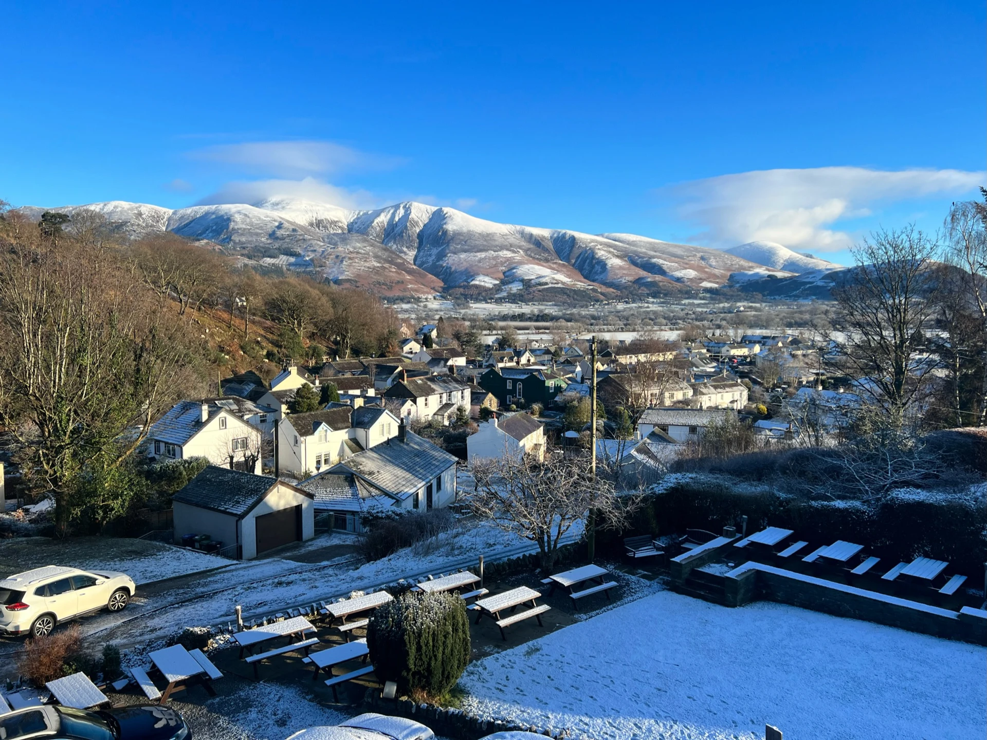 The snowy village of Braithwaite Village in Keswick with rolling snowy mountains in the distance.