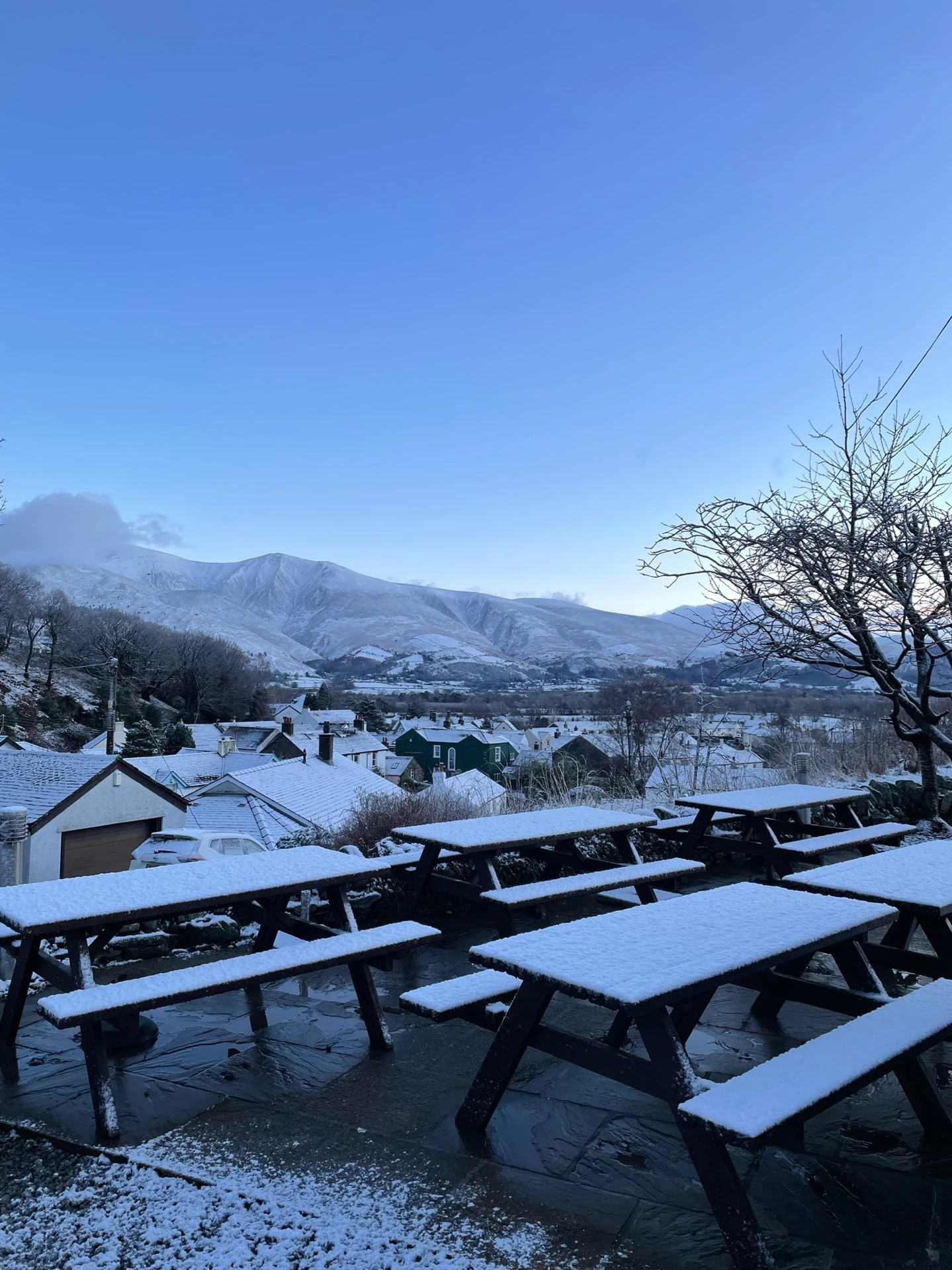 The Coledale Inn's outdoor garden during a sunrise in winter with benches covered in snow and views of a snowy village in the background