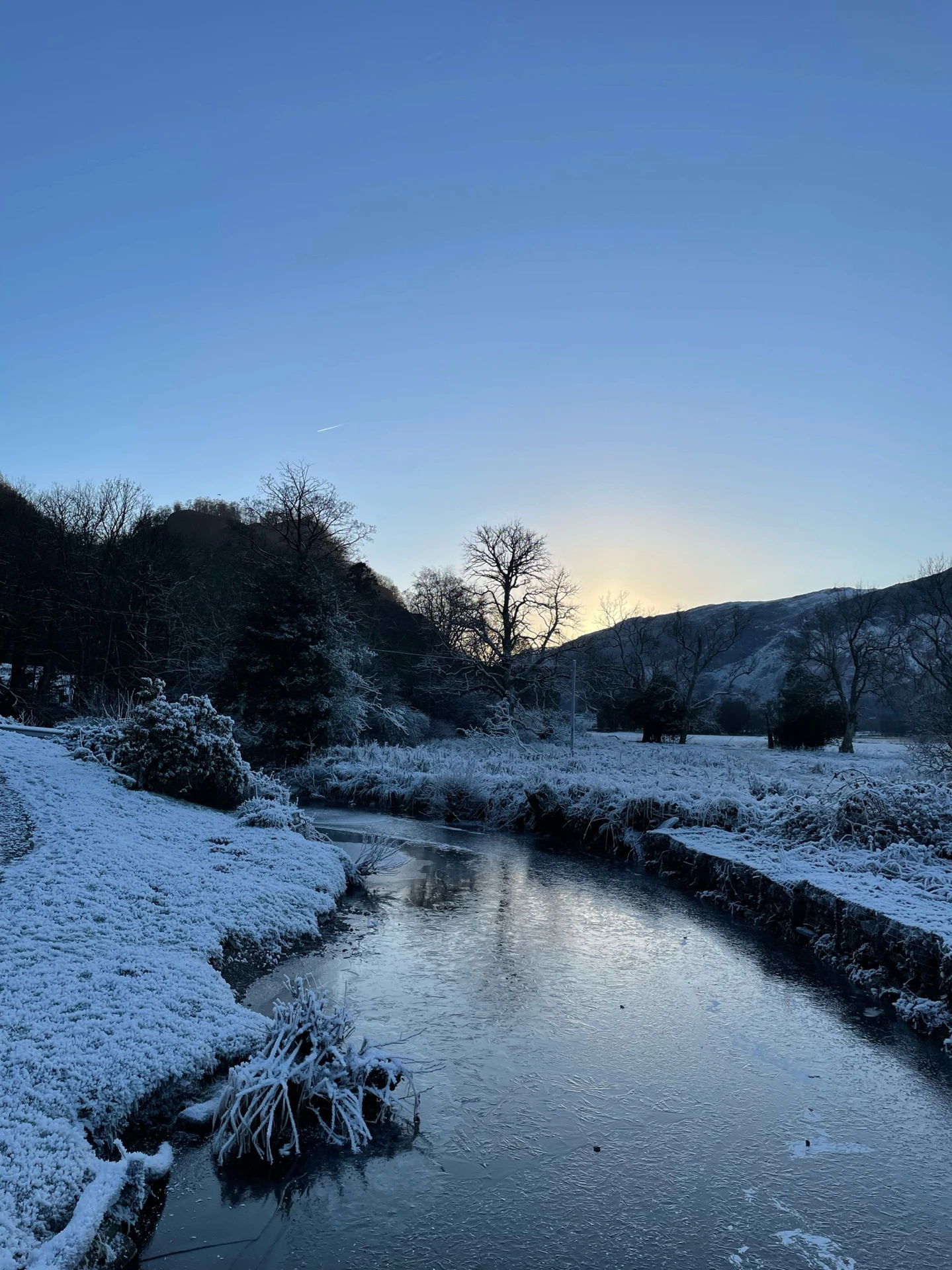 An icy lake in the lake district at sunrise with snowy hills surrounding.