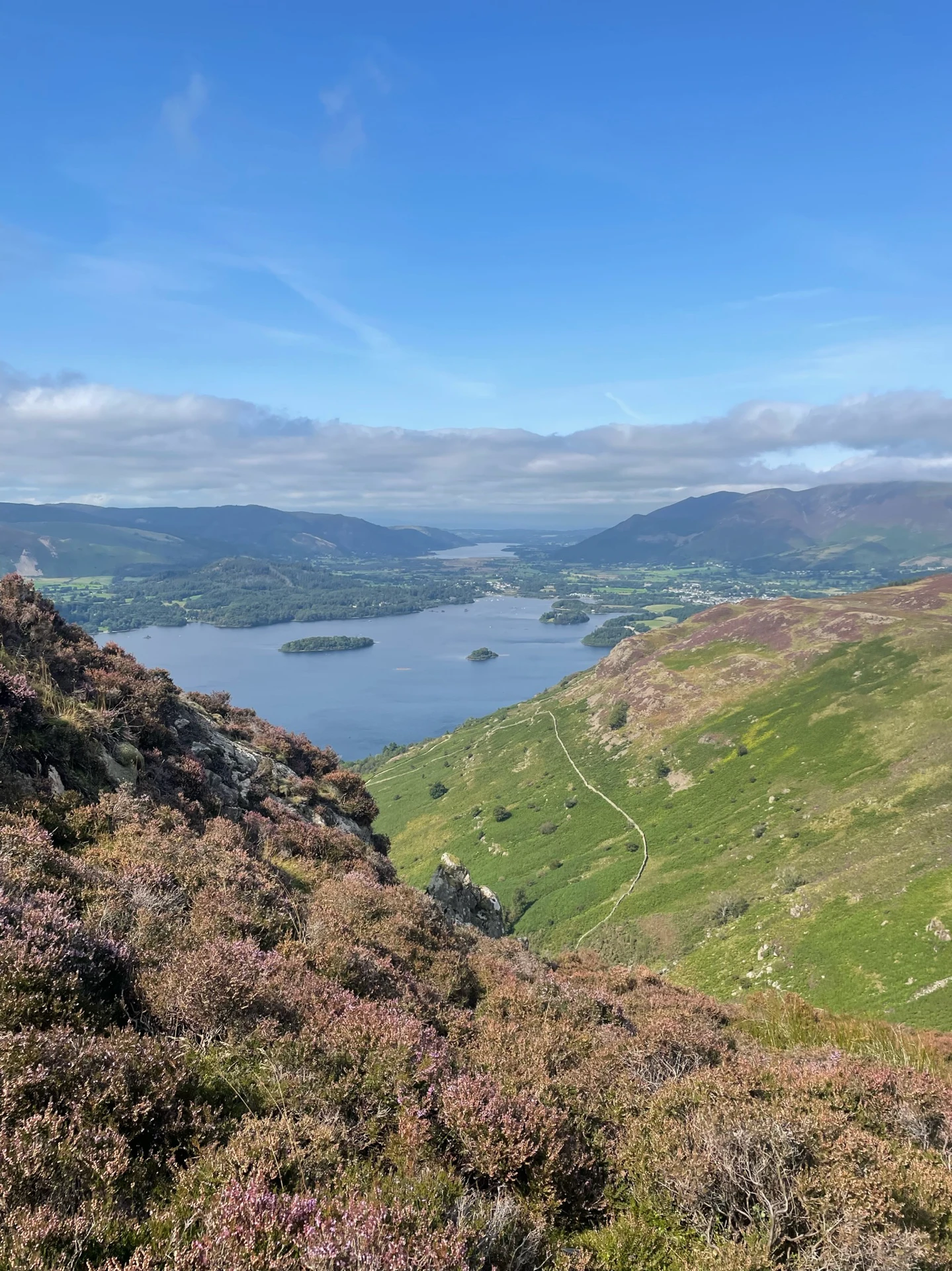 Rolling lush hills in the Lake District around Braithwaite Village under a sunny blue sky.
