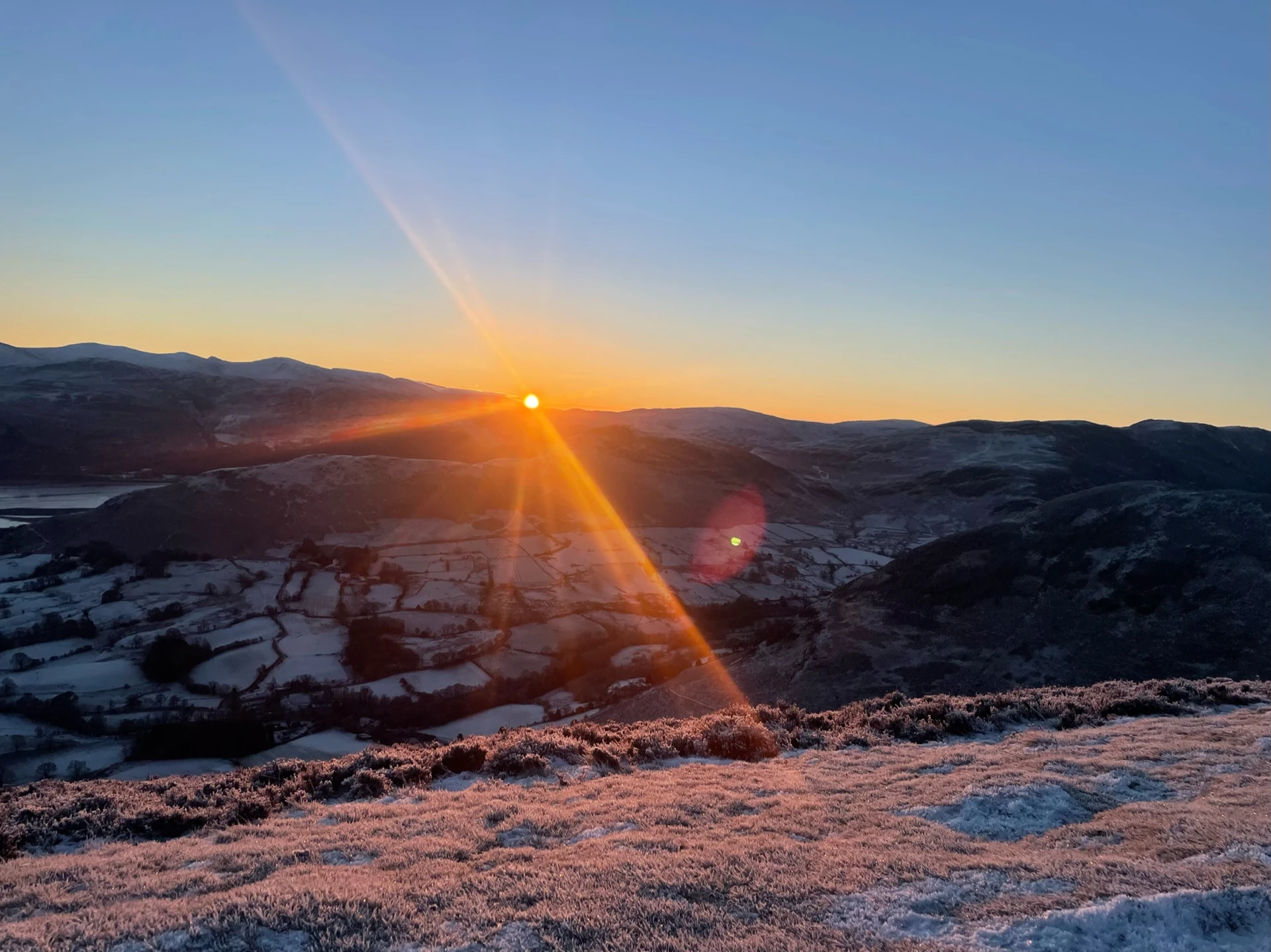 Sun setting over the icy rolling hills around Braithwaite Village in the Lake District.