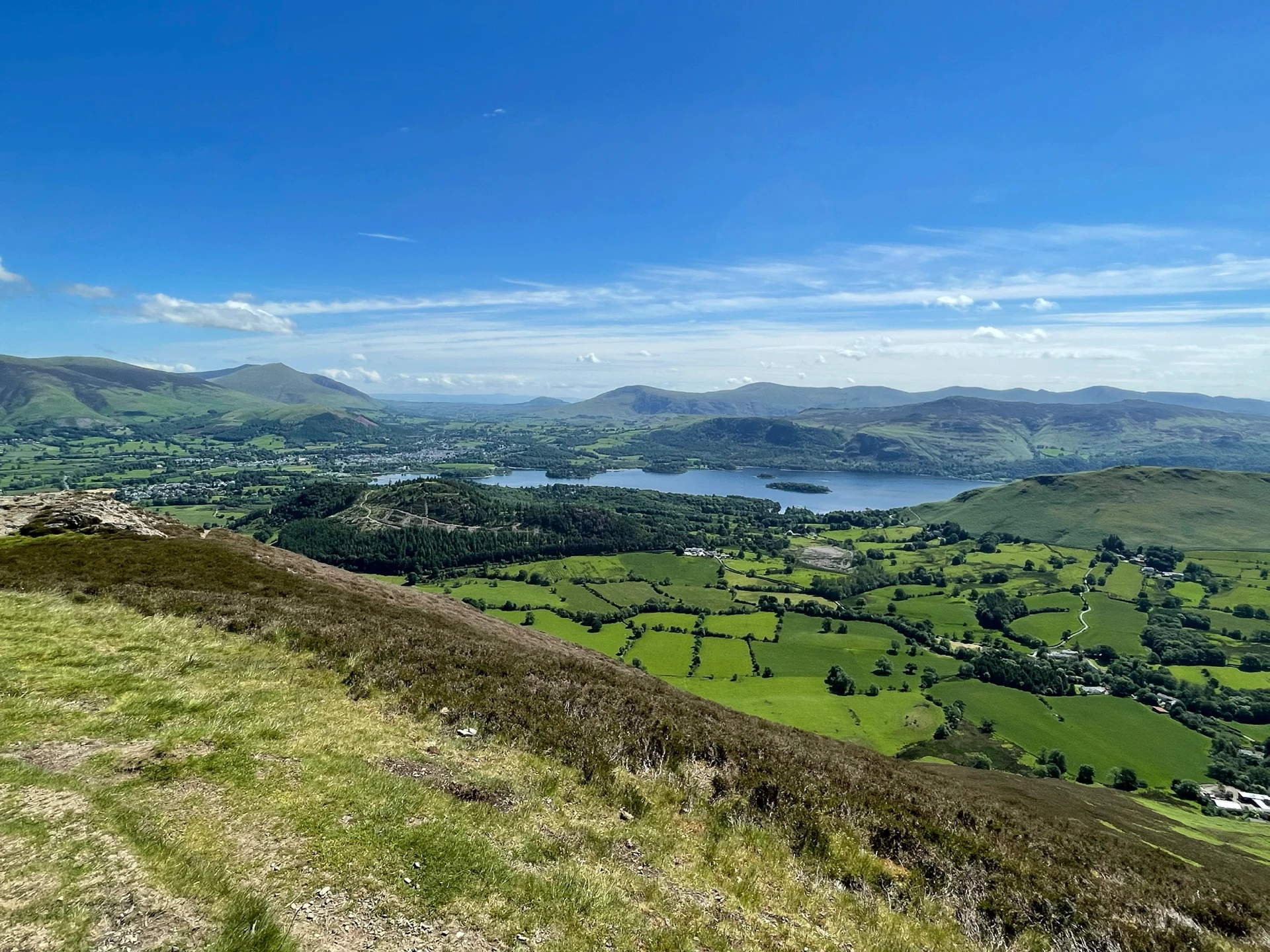 Rolling lush hills in the Lake District around Braithwaite Village under a sunny blue sky.
