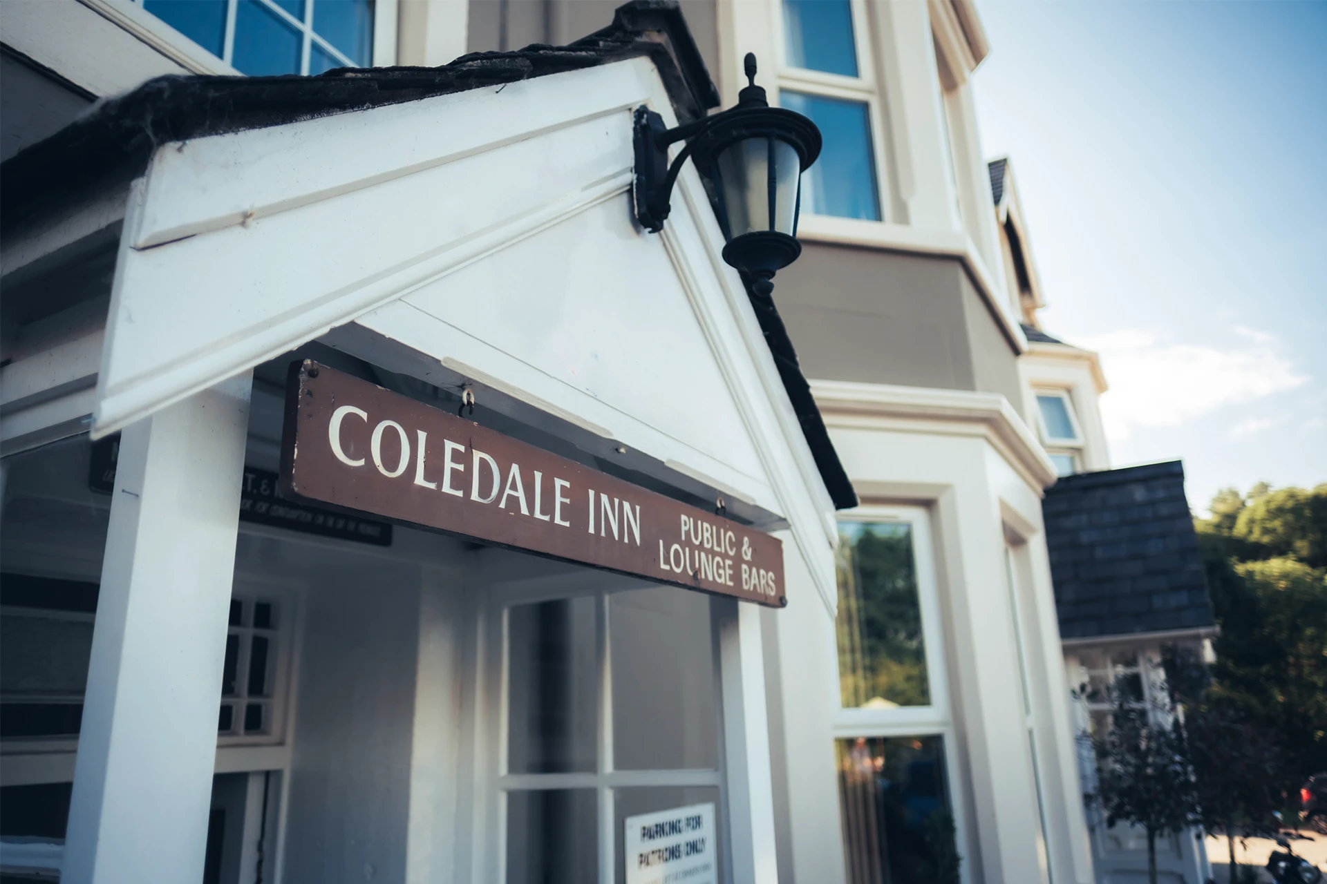 Exterior view of a building with a sign that reads COLLINGDALE B N and B. The structure features white trim and tall windows, with a lantern mounted above the entrance. Trees and blue sky are visible in the background.