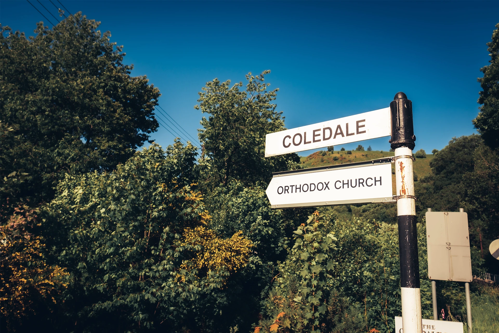 A signpost surrounded by trees points toward Coldwells and Stretton Church under a clear blue sky.