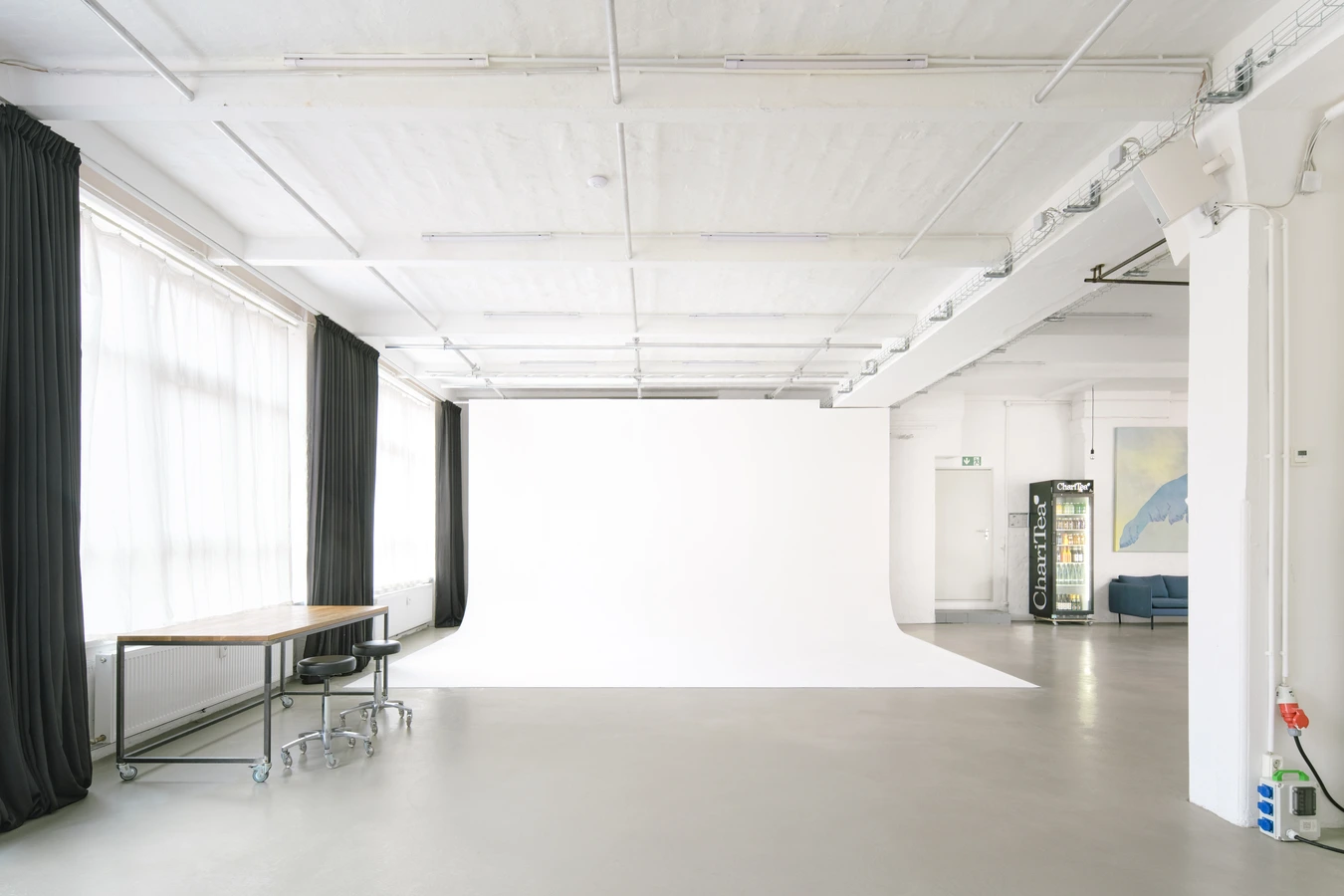 Shootingbereich von Studio 4 mit weißer Backsteinwand, großer Fensterfront, blickdichten Vorhängen und Betonboden im Industrie-Look
