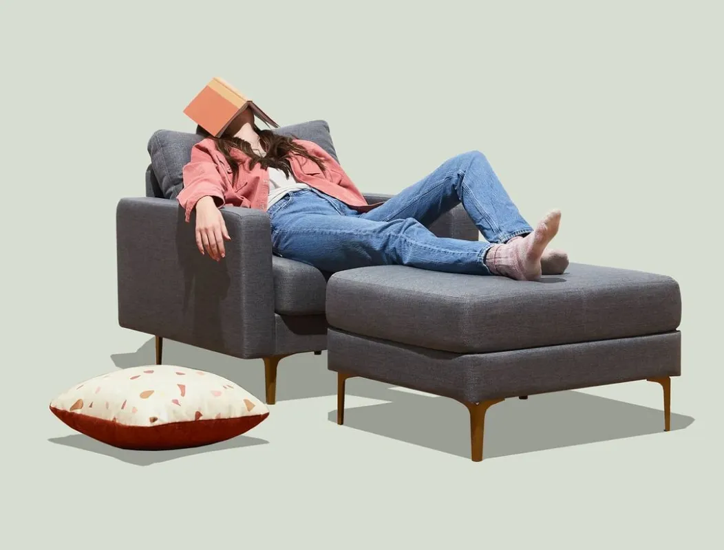 A woman is laying on a couch with a book on her head.