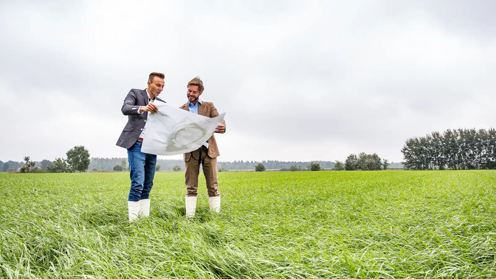 Twee mannen staan met een bouwtekening in een groen grasveld