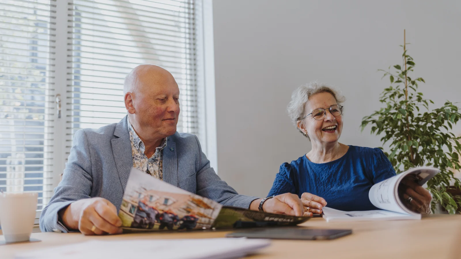 Twee oude mensen zitten samen aan een tafel vol met magazines
