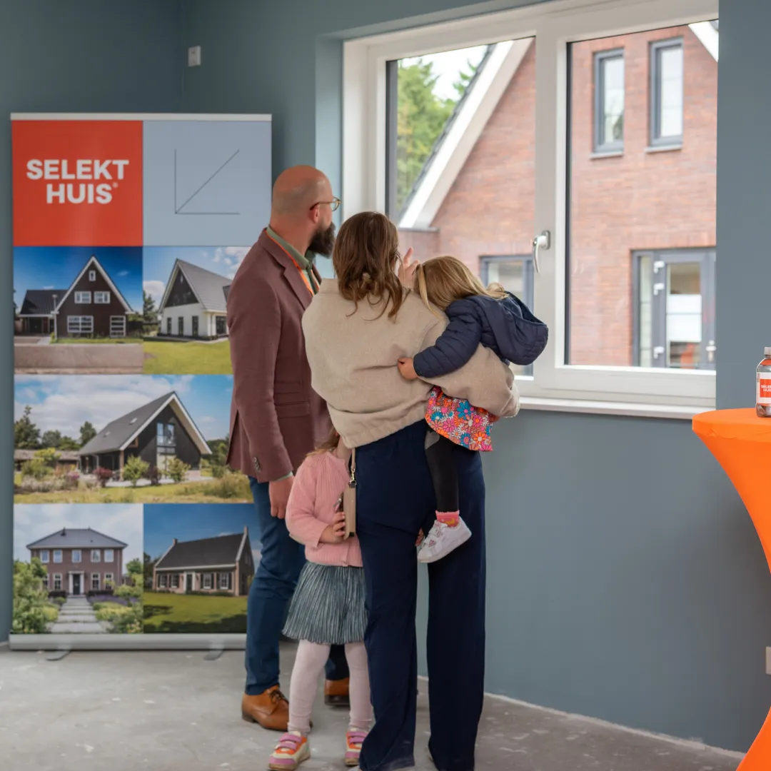 Twee volwassen en 2 kinderen kijken uit het raam naar een woning