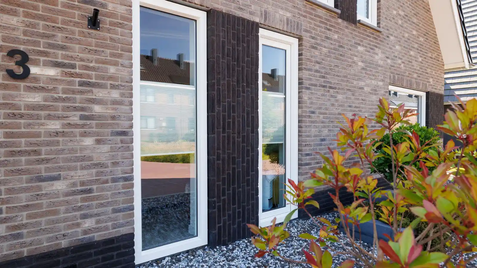 Twee grote ramen met donkere rechtopstaande stenen in het midden