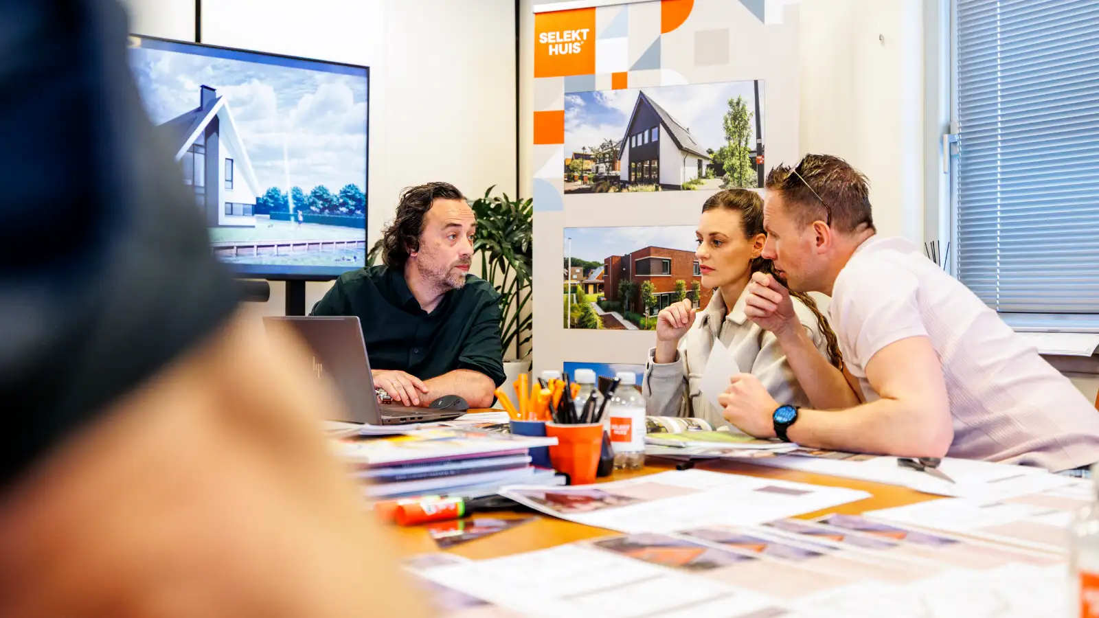 Drie mensen zitten aan een tafel kijkend naar een laptop