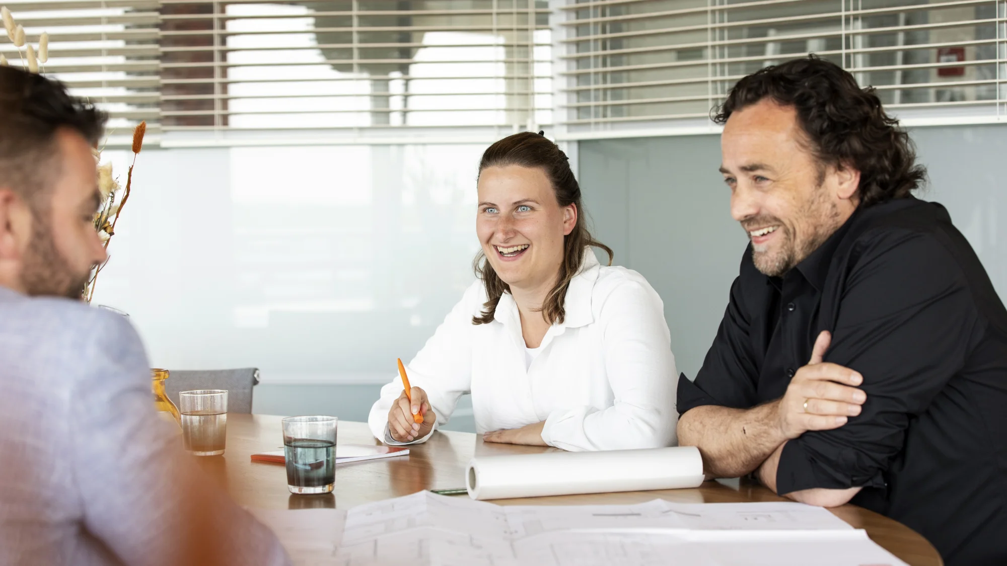 Twee mannen en een vrouw zitten aan een tafel te overleggen