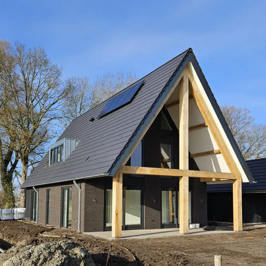 Vrijstaande woning met overkapping en houten gebinten en donkere stenen.