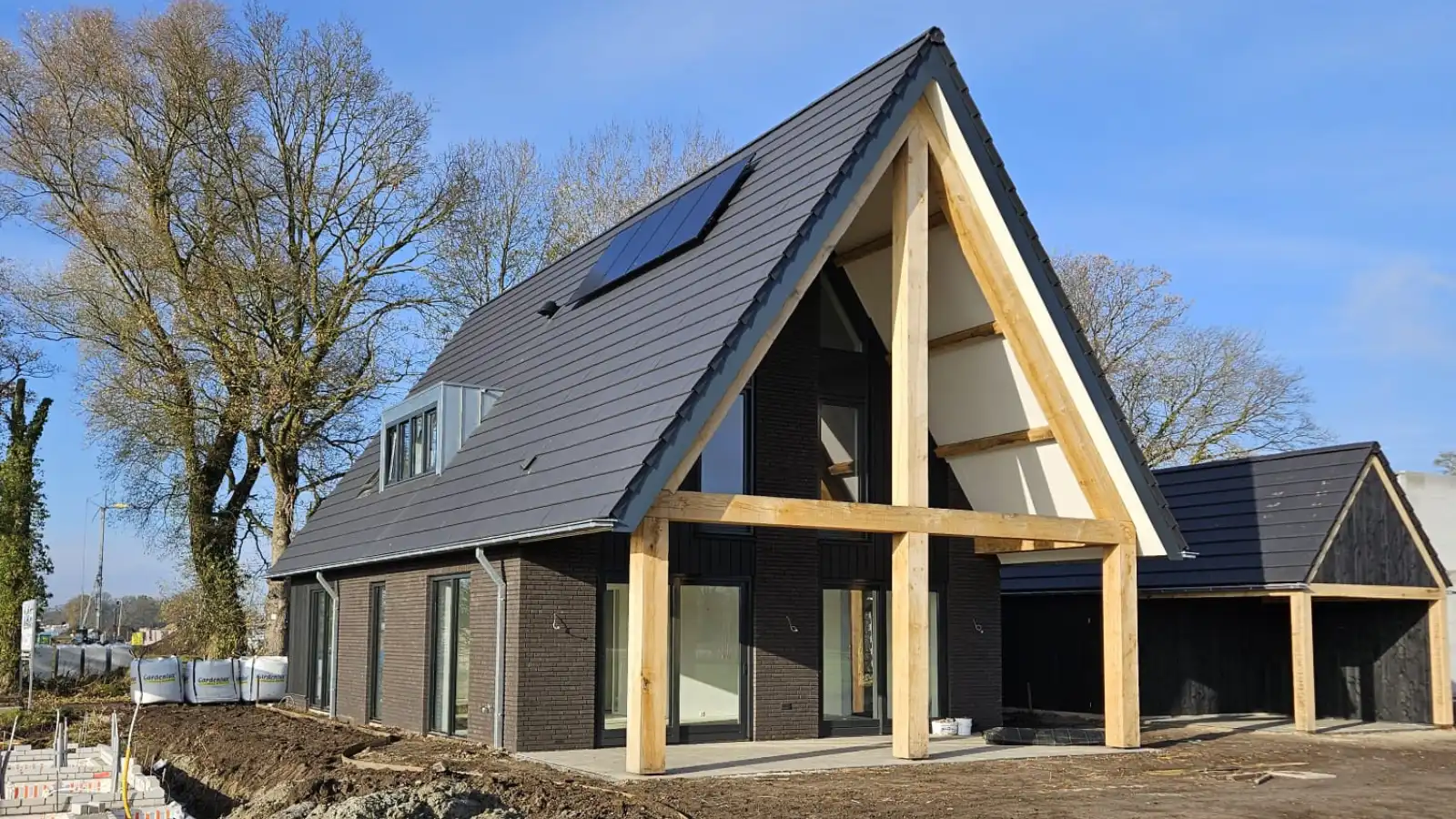 Vrijstaande woning met overkapping en houten gebinten en donkere stenen.