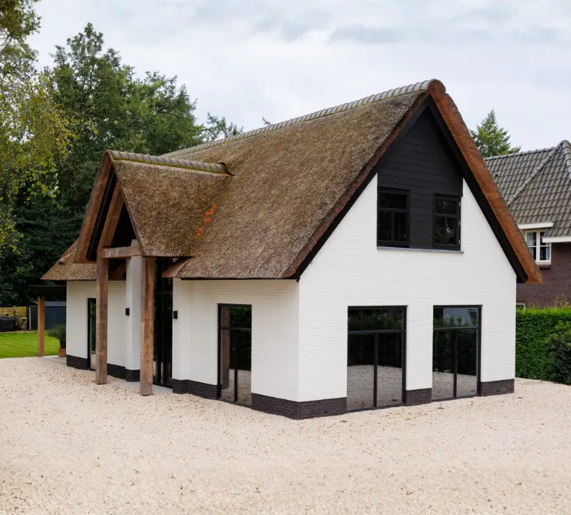Vooraanzicht van een vrijstaande witte woning met rieten kap en risaliet
