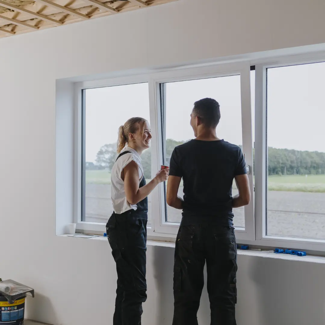 Man en vrouw staan bij een raam en kijken naar buiten in een nog af te bouwen huis