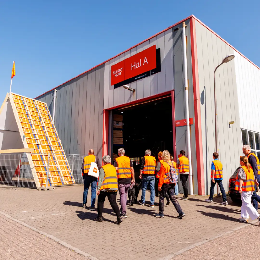 Een groep mensen met veiligheidshesje aan lopen een grote hal in