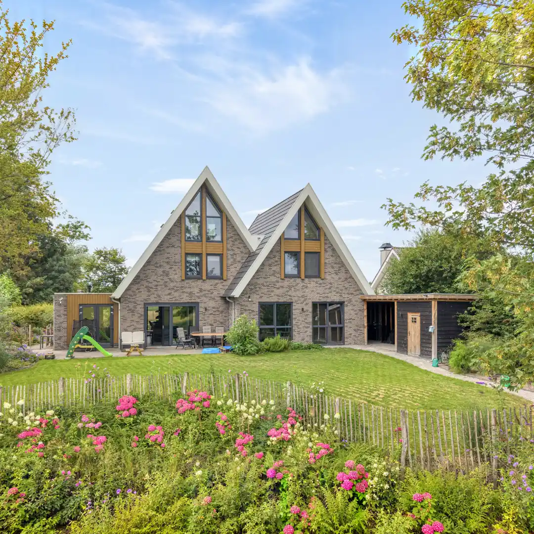 Acherzijde vrijstaande woning het aanbouw. Grijze gevelstenen en houten gevelbekleding