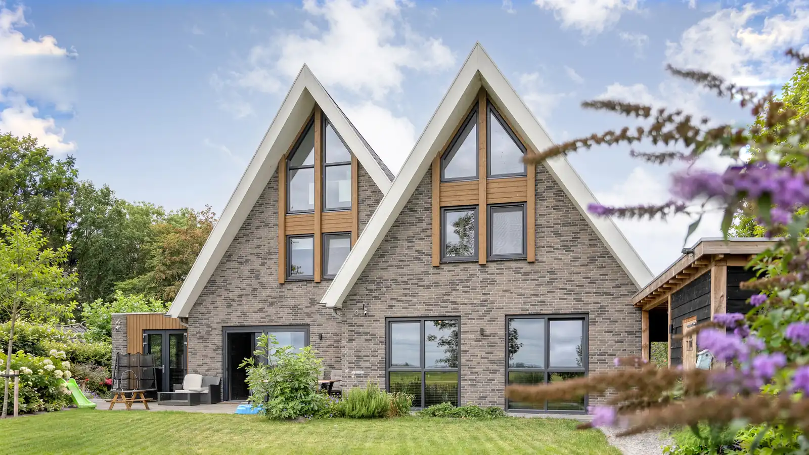 Achterzijde vrijstaande woning met twee gevelpunten. Grijze gevelstenen en houten gevelbekleding