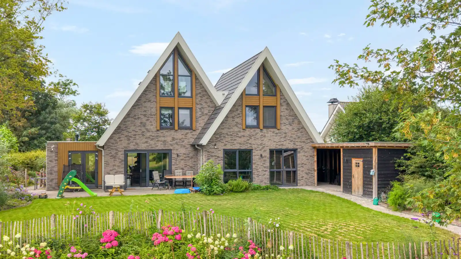 Achterzijde vrijstaande woning met twee gevelpunten. Grijze gevelstenen en houten gevelbekleding