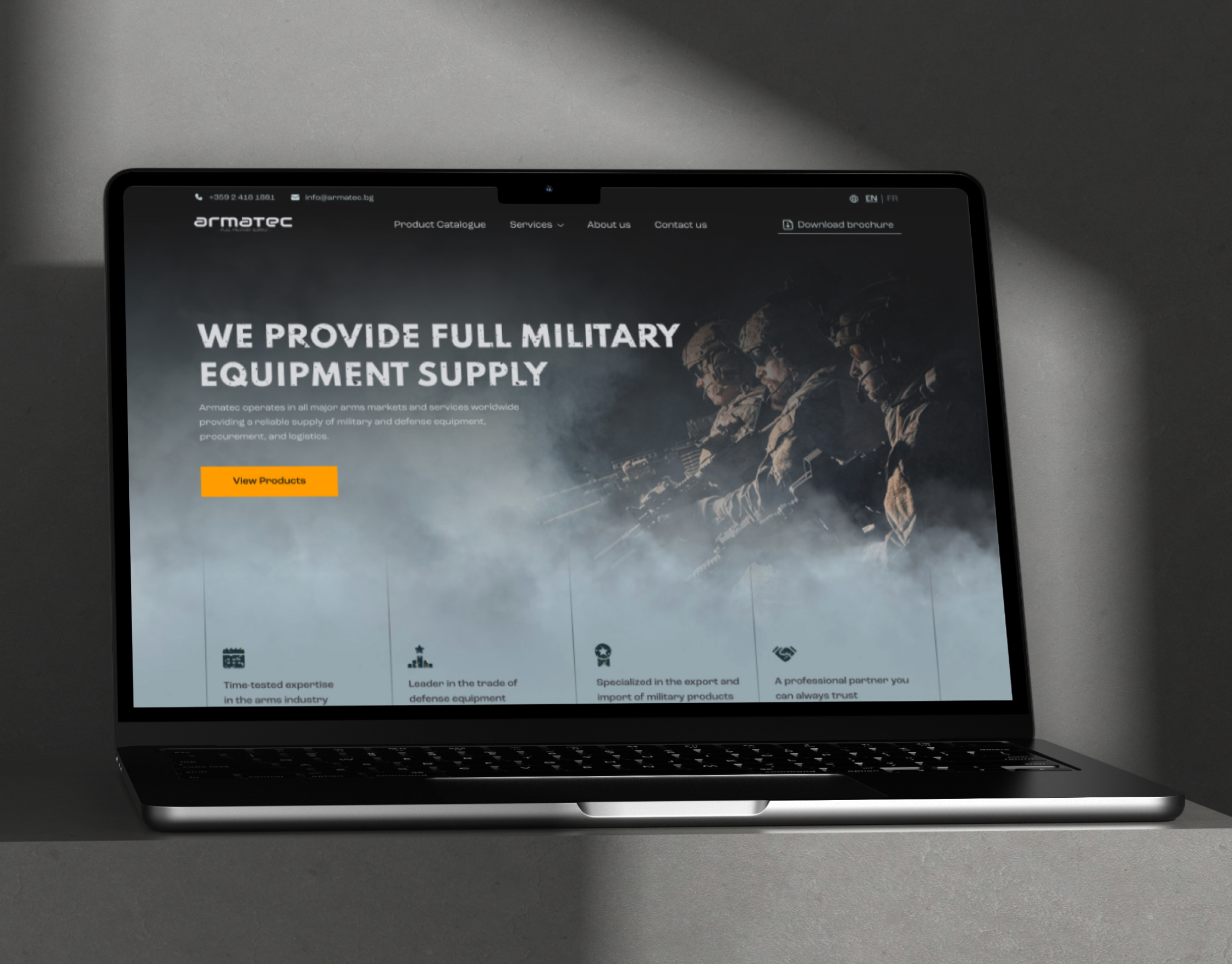Armatec homepage on a laptop screen, with the dark soldier hero image and a yellow View Products button